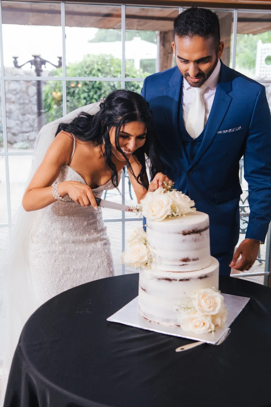 Bride and groom laughing while cutting their semi-naked wedding cake at reception — wedding photography Niagara Region by Captivate Photo+Cinema