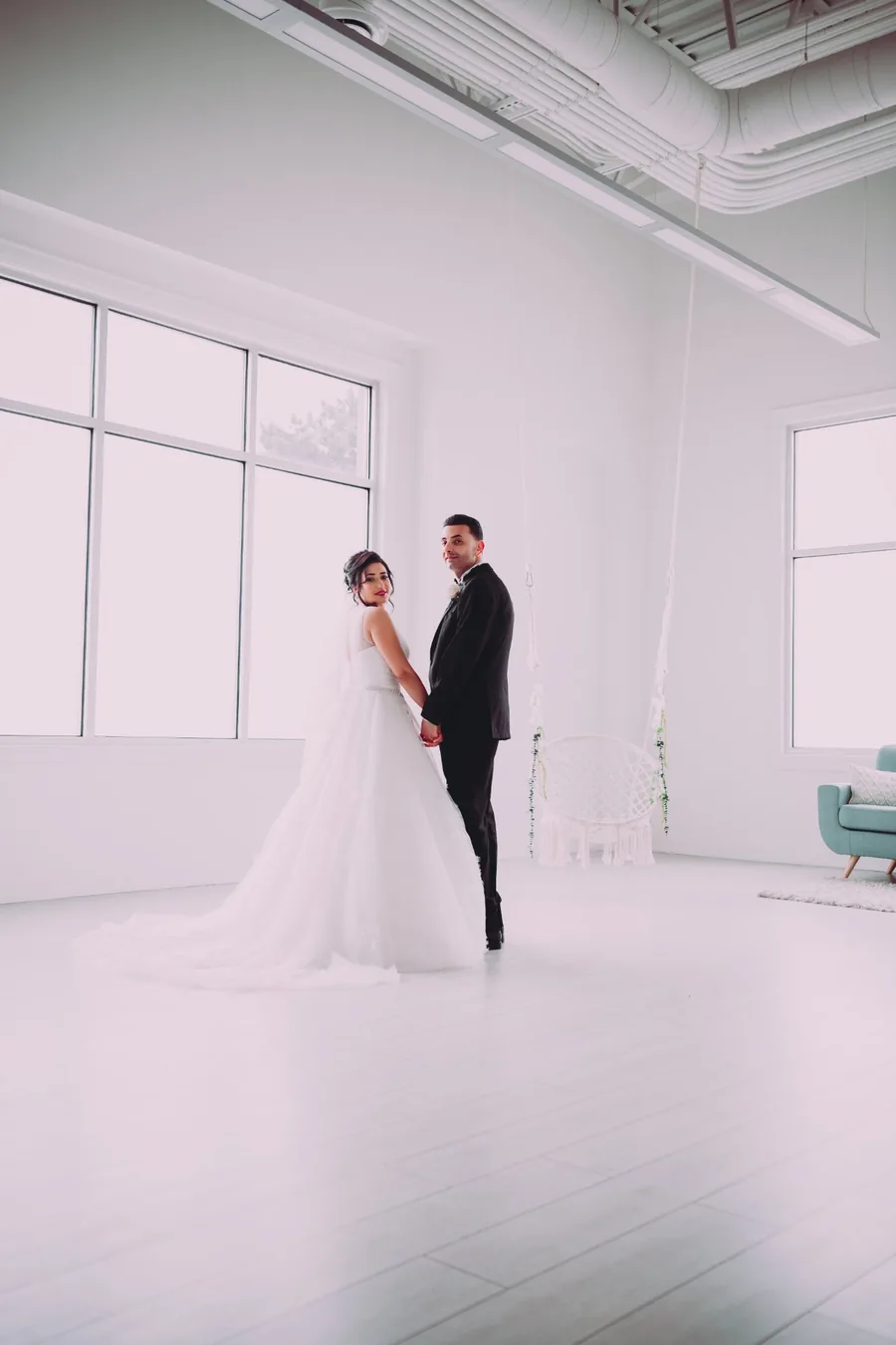 Bride and groom holding hands in a bright all-white studio space — elegant full length wedding portrait photography Niagara by Captivate Photo+Cinema