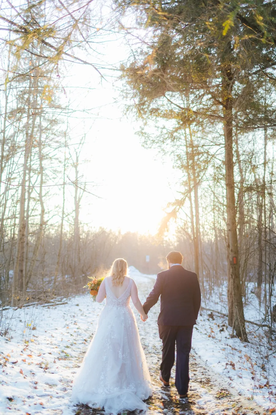Bride and groom walking hand in hand through a snowy forest at sunset — winter wedding photography Ontario by Captivate Photo+Cinema