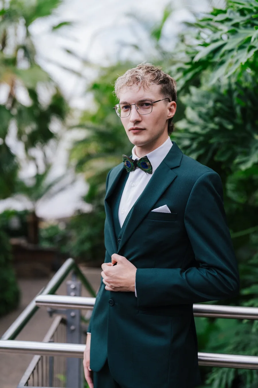 Groom in teal suit with peacock feather bowtie and glasses posing in a greenhouse — unique groom portrait wedding photography Niagara by Captivate Photo+Cinema