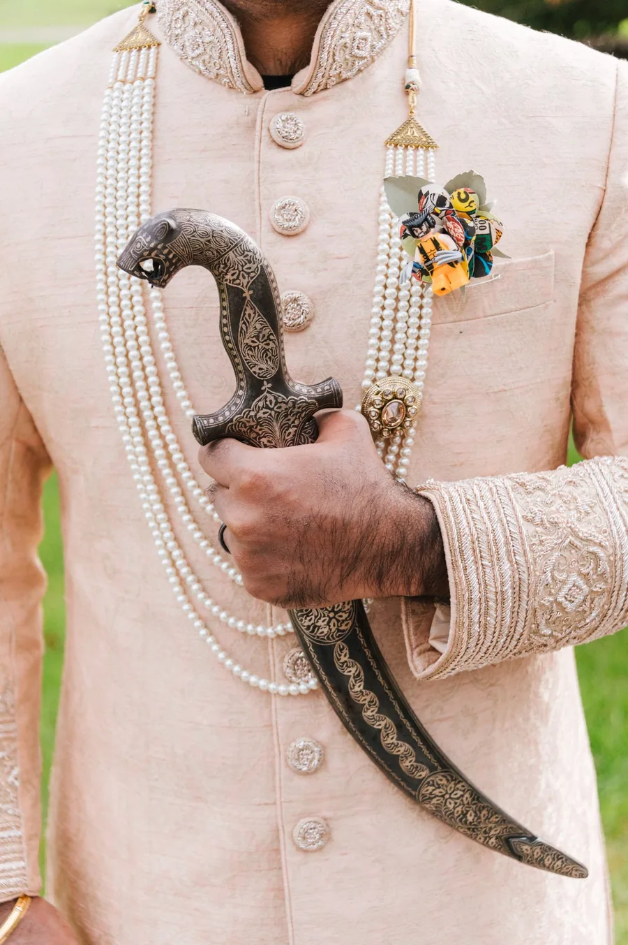 Detail shot of South Asian groom in cream sherwani holding ceremonial kirpan with pearl garlands — multicultural wedding photography Ontario by Captivate Photo+Cinema